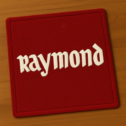 Red Raymond logo rug top view showing white brand text on hand-tufted rug placed flat on wooden surface.